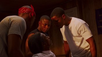 Movie still from “Red Hook Summer” (2012), directed by Spike Lee – A group of men standing around a woman in a room; Medium shot, Low angle