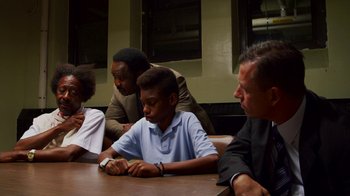 Movie still from “Red Hook Summer” (2012), directed by Spike Lee – A group of people sitting at a table looking at a cell phone; Medium shot, High angle