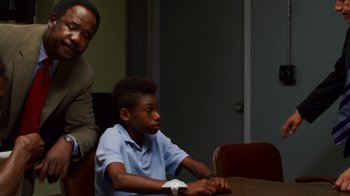 Movie still from “Red Hook Summer” (2012), directed by Spike Lee – A young boy sitting at a table with a remote control; Medium shot, Over the shoulder angle