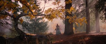 A woman in a long blue dress holding an arrow in the woods