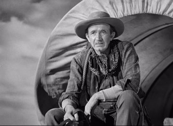 Movie still from “Red River” (1948), directed by Howard Hawks – An old man sitting on a chair with an open umbrella; Medium shot, Low angle