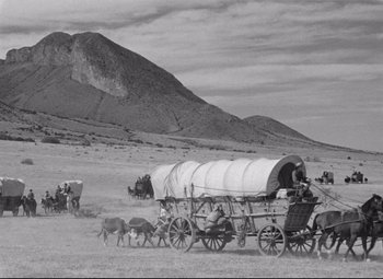 Movie still from “Red River” (1948), directed by Howard Hawks – An old photo of a covered wagon in the desert; Extreme Wide shot, High angle
