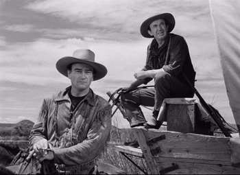 Movie still from “Red River” (1948), directed by Howard Hawks – A couple of men sitting next to each other on a bench; Medium shot, Low angle