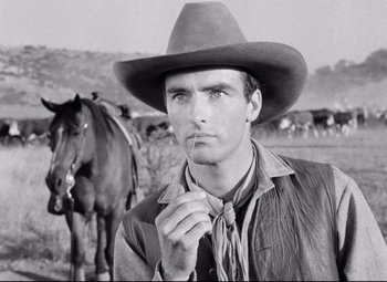 Movie still from “Red River” (1948), directed by Howard Hawks – A man wearing a cowboy hat standing in front of a herd of horses; Close Up shot, Low angle