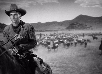Movie still from “Red River” (1948), directed by Howard Hawks – A man on a horse with a bunch of cows in the background; Medium shot, Low angle