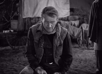 Movie still from “Red River” (1948), directed by Howard Hawks – A black and white photo of a man sitting on the ground; Medium shot, Over the shoulder angle