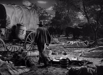 Movie still from “Red River” (1948), directed by Howard Hawks – A man standing next to a wagon in a field; Wide shot, High angle
