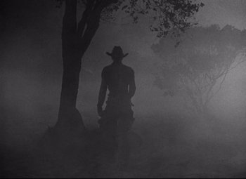 Movie still from “Red River” (1948), directed by Howard Hawks – A man in a cowboy hat standing next to a tree in the fog; Wide shot, Low angle