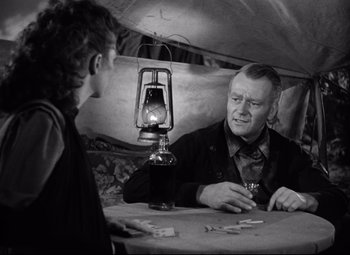 Movie still from “Red River” (1948), directed by Howard Hawks – A man sitting at a table with another man in front of him; Medium shot, Over the shoulder angle