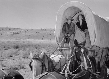 Movie still from “Red River” (1948), directed by Howard Hawks – A couple of people sitting in a covered wagon on top of horses; Wide shot, Low angle