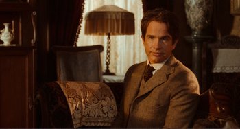 Movie still from “Reds” (1981), directed by Warren Beatty – A man sitting in a chair in front of a lamp; Medium shot, Over the shoulder angle