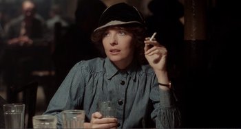 Movie still from “Reds” (1981), directed by Warren Beatty – A woman in a hat smoking a cigarette and drinking a beverage; Close Up shot, Over the shoulder angle