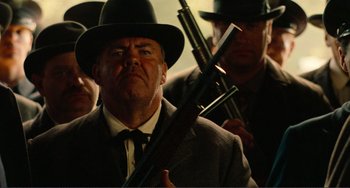 Movie still from “Reds” (1981), directed by Warren Beatty – A man in a suit and a hat holding a rifle; Medium shot, Low angle