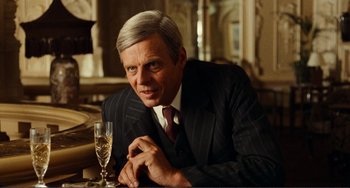 Movie still from “Reds” (1981), directed by Warren Beatty – An older man sitting at a table with a glass of champagne; Close Up shot, Over the shoulder angle