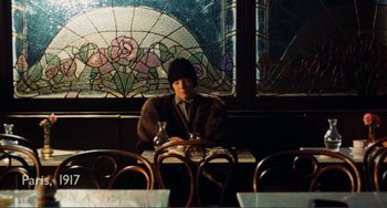 Movie still from “Reds” (1981), directed by Warren Beatty – A man sitting at a table in front of a stained glass window; Wide shot, High angle