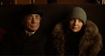 Movie still from “Reds” (1981), directed by Warren Beatty – An older man and a younger woman sitting next to each other; Medium shot, Low angle