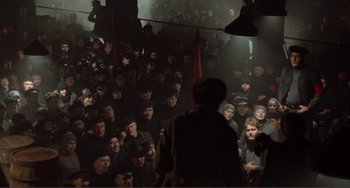 Movie still from “Reds” (1981), directed by Warren Beatty – A group of people sitting in a dark room; Wide shot, High angle