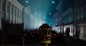 A yellow tram is going down the street at night