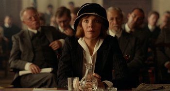 Movie still from “Reds” (1981), directed by Warren Beatty – A woman sitting at a table in front of other people; Medium shot, Low angle