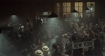 Movie still from “Reds” (1981), directed by Warren Beatty – A group of people sitting in a room holding signs; Extreme Wide shot, High angle