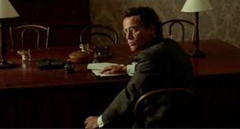 Movie still from “Reds” (1981), directed by Warren Beatty – A man sitting at a table with a book in front of him; Medium shot, Over the shoulder angle