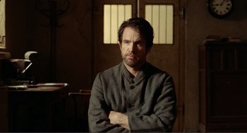 Movie still from “Reds” (1981), directed by Warren Beatty – A man with his arms crossed in front of a door; Medium shot, Over the shoulder angle