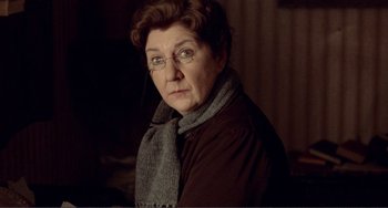 Movie still from “Reds” (1981), directed by Warren Beatty – An older woman wearing glasses and wearing a scarf; Close Up shot, Over the shoulder angle