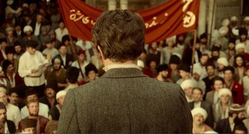 Movie still from “Reds” (1981), directed by Warren Beatty – A man in a suit is standing in front of a group of people; Wide shot, Over the shoulder angle