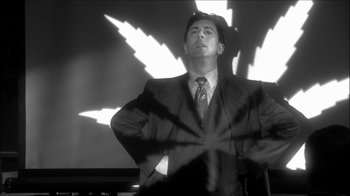 Movie still from “Reefer Madness: The Movie Musical” (2005), directed by Andy Fickman – A black and white photo of a man in a suit and tie; Medium shot, Low angle