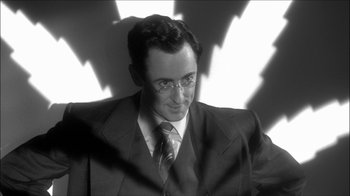 Movie still from “Reefer Madness: The Movie Musical” (2005), directed by Andy Fickman – A black and white photo of a man wearing a suit and tie; Close Up shot, Low angle