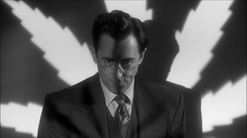 Movie still from “Reefer Madness: The Movie Musical” (2005), directed by Andy Fickman – A black and white photo of a man in a suit and tie; Close Up shot, Low angle