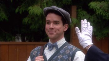 Movie still from “Reefer Madness: The Movie Musical” (2005), directed by Andy Fickman – A man wearing a bow tie and a hat waving; Medium shot, Over the shoulder angle