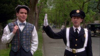 Movie still from “Reefer Madness: The Movie Musical” (2005), directed by Andy Fickman – A man in a suit and tie standing next to another man in a suit and tie; Medium shot, Over the shoulder angle