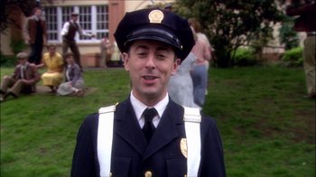 Movie still from “Reefer Madness: The Movie Musical” (2005), directed by Andy Fickman – A man in a police uniform standing in front of a group of people; Medium shot, High angle