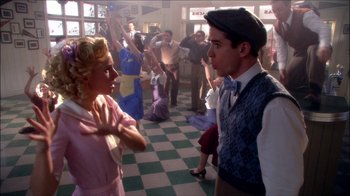 Movie still from “Reefer Madness: The Movie Musical” (2005), directed by Andy Fickman – A man and a woman are talking to each other in front of a crowd; Medium shot, High angle