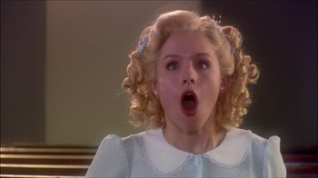 Movie still from “Reefer Madness: The Movie Musical” (2005), directed by Andy Fickman – A young girl with blonde curly hair wearing a blue dress and pigtails; Close Up shot, Low angle