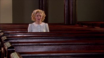 Movie still from “Reefer Madness: The Movie Musical” (2005), directed by Andy Fickman – A woman sitting in a church peering over a row of pews; Wide shot, Over the shoulder angle