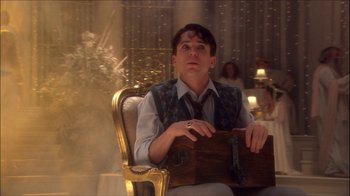 Movie still from “Reefer Madness: The Movie Musical” (2005), directed by Andy Fickman – A man sitting in a chair holding a suitcase; Medium shot, Low angle