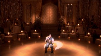 Movie still from “Reefer Madness: The Movie Musical” (2005), directed by Andy Fickman – A man sitting on a chair holding a guitar in front of candles; Extreme Wide shot, High angle