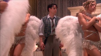 Movie still from “Reefer Madness: The Movie Musical” (2005), directed by Andy Fickman – A man standing next to a couple of women in angel wings; Medium shot, Over the shoulder angle