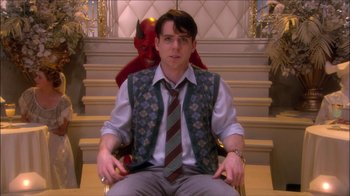 Movie still from “Reefer Madness: The Movie Musical” (2005), directed by Andy Fickman – A man sitting in a chair with a red demon sitting behind him; Medium shot, Over the shoulder angle