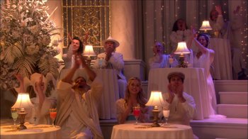 Movie still from “Reefer Madness: The Movie Musical” (2005), directed by Andy Fickman – A group of people sitting at a table with lamps; Wide shot, High angle