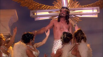 Movie still from “Reefer Madness: The Movie Musical” (2005), directed by Andy Fickman – A man with a crown of hair is being held up by a group of women; Wide shot, High angle