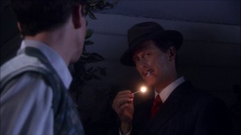 Movie still from “Reefer Madness: The Movie Musical” (2005), directed by Andy Fickman – A man wearing a suit and tie holding a light up cigarette; Close Up shot, Over the shoulder angle