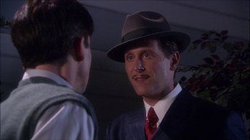 Movie still from “Reefer Madness: The Movie Musical” (2005), directed by Andy Fickman – A man wearing a suit and a hat talking to another man; Close Up shot, Over the shoulder angle