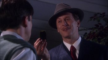 Movie still from “Reefer Madness: The Movie Musical” (2005), directed by Andy Fickman – A man wearing a suit and a hat holding a piece of cake; Close Up shot, Over the shoulder angle