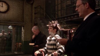 Movie still from “Reefer Madness: The Movie Musical” (2005), directed by Andy Fickman – A man with a crown on his head is sitting in a chair; Medium shot, High angle