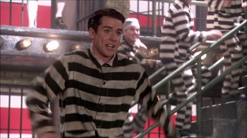 Movie still from “Reefer Madness: The Movie Musical” (2005), directed by Andy Fickman – A man in a striped shirt and black and white striped shirt standing in front of some stairs; Medium shot, Over the shoulder angle