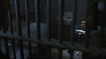 Movie still from “Reindeer Games” (2000), directed by John Frankenheimer – A man sitting on a bed next to a jail cell; Wide shot, High angle