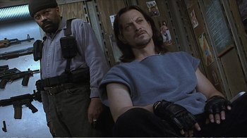 Movie still from “Reindeer Games” (2000), directed by John Frankenheimer – A man sitting in a chair with a gun in his hand; Medium shot, Over the shoulder angle